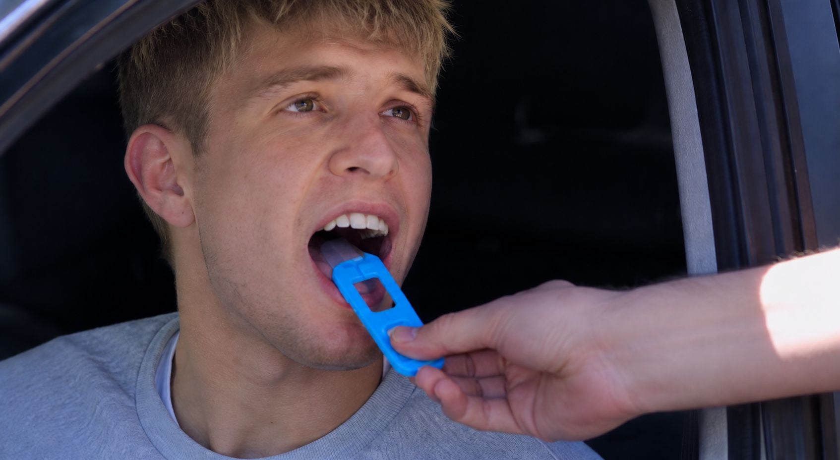 A law enforcement officer administers a roadside oral fluid swab test to a driver seated in a car